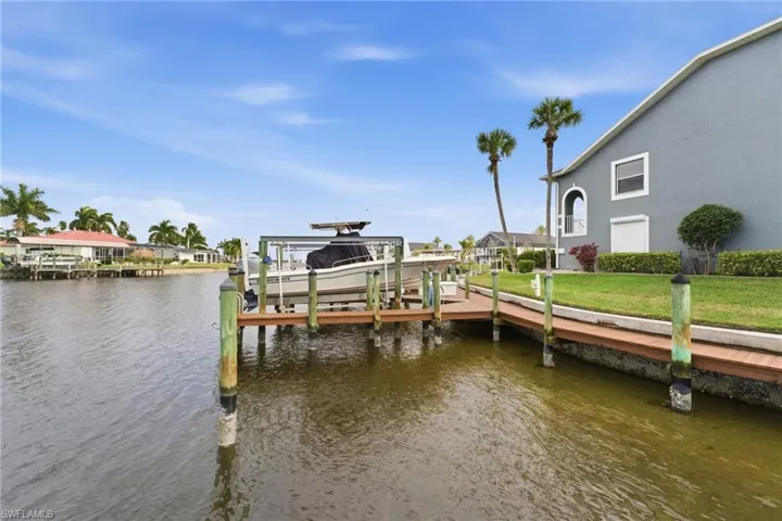 Dock with boat lift, a water view, and a yard