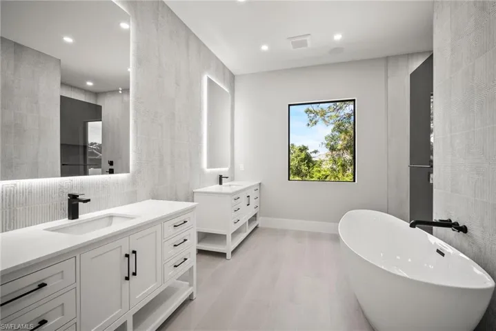Bathroom with tile walls, two vanities, recessed lighting, a freestanding bath, and light wood-style floors