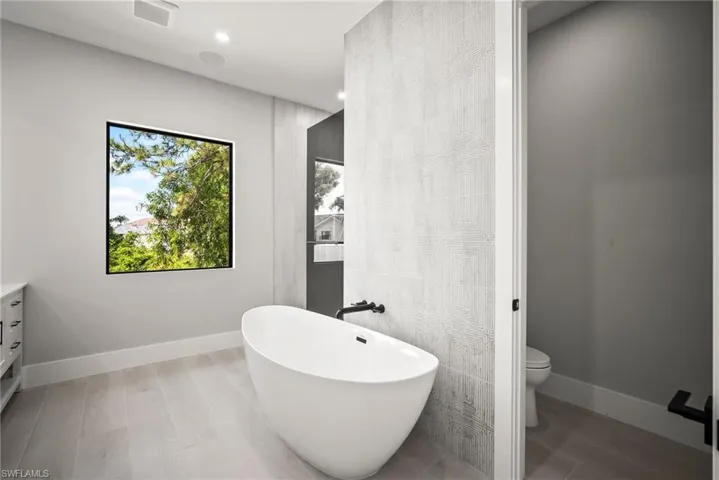 Bathroom featuring vanity, a soaking tub, tile walls, light wood-style flooring, and recessed lighting