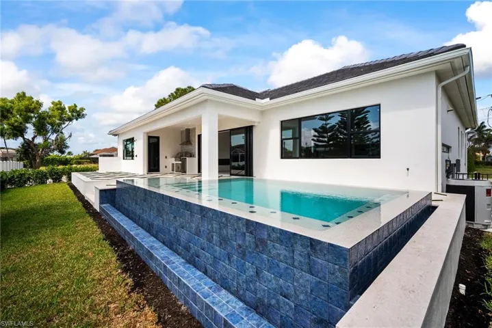 Rear view of property featuring a patio area, stucco siding, an infinity pool, and a yard