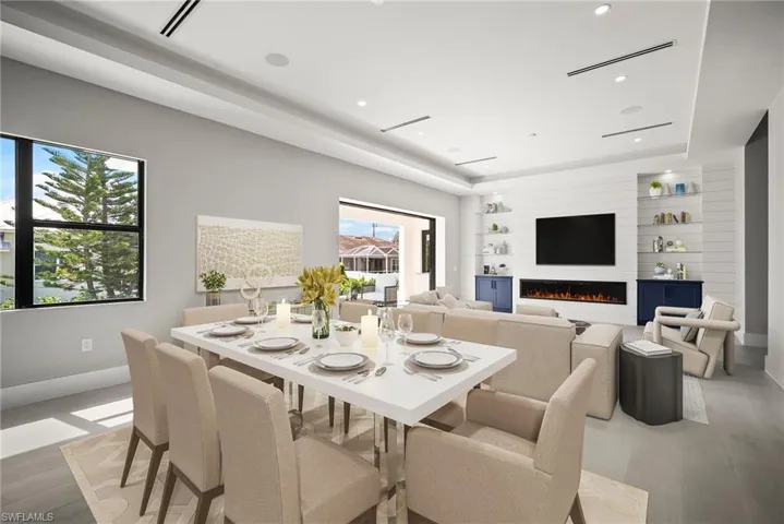Dining space with a lit fireplace, a raised ceiling, light wood-type flooring, and recessed lighting