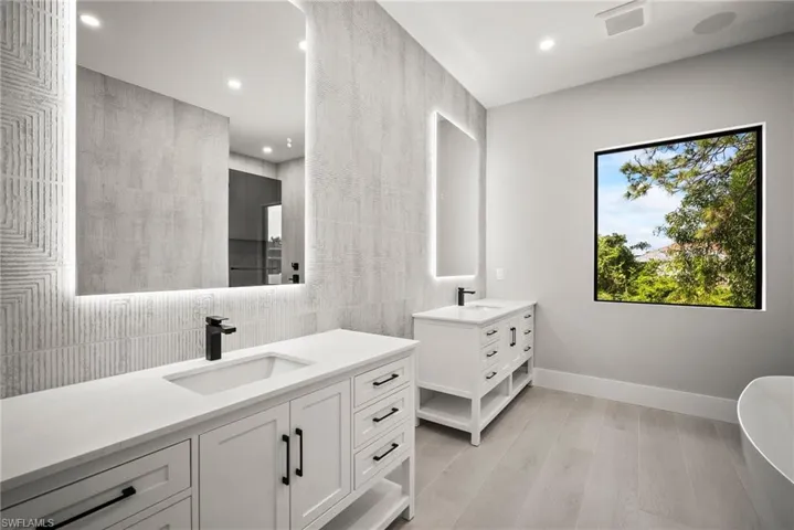 Bathroom featuring tile walls, two vanities, a freestanding bath, recessed lighting, and light wood finished floors