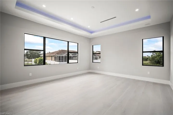 Empty room featuring a tray ceiling, light wood-type flooring, and recessed lighting