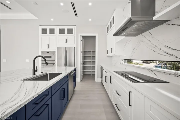 Kitchen with blue cabinetry, white cabinetry, wall chimney exhaust hood, and recessed lighting