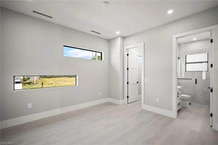 Unfurnished bedroom featuring multiple windows, light wood-type flooring, ensuite bathroom, recessed lighting, and a spacious closet