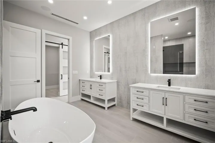 Full bath with tile walls, a freestanding tub, recessed lighting, two vanities, and light wood finished floors
