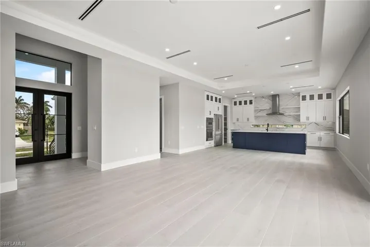 Unfurnished living room with recessed lighting, french doors, light wood finished floors, and a tray ceiling
