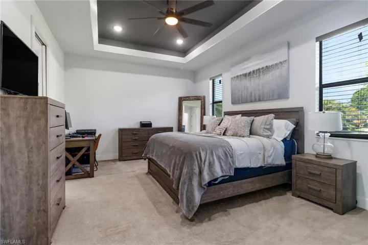 Bedroom featuring light colored carpet, a tray ceiling, recessed lighting, and ceiling fan