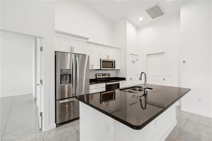 Kitchen featuring appliances with stainless steel finishes, sink, a high ceiling, white cabinets, and a kitchen island with sink