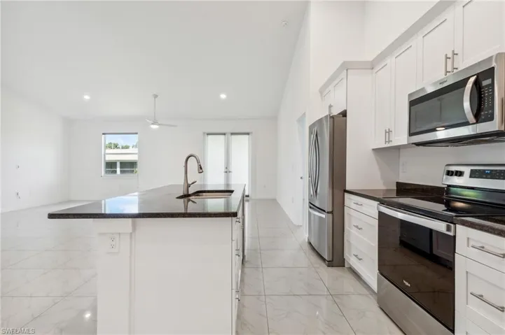 Kitchen featuring a kitchen island with sink, stainless steel appliances, sink, vaulted ceiling, and white cabinetry
