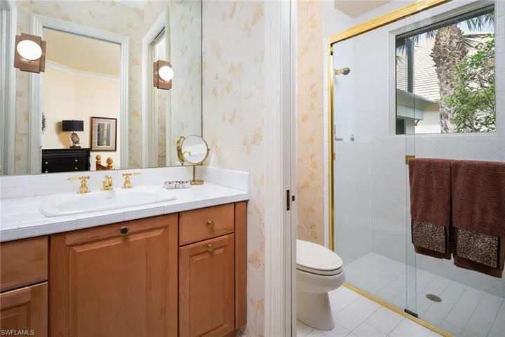 Bathroom featuring vanity, wallpapered walls, a shower stall, and light tile patterned floors