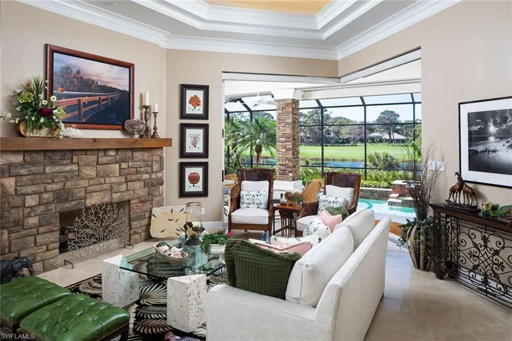 Living area featuring a sunroom, crown molding, a stone fireplace, and a tray ceiling