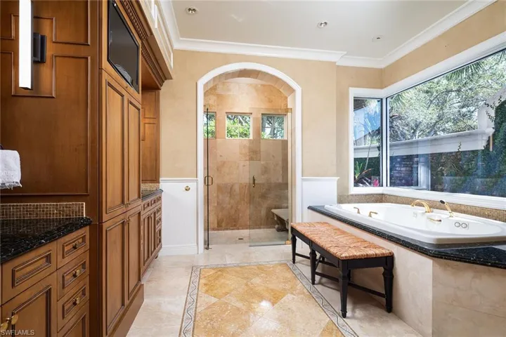 Full bath with ornamental molding, a bath, a stall shower, a wainscoted wall, and vanity