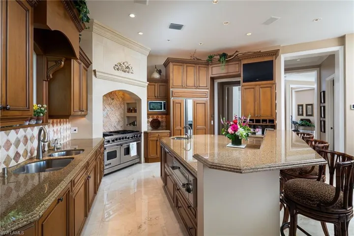 Kitchen with wood finish cabinetry, dark stone countertops, tasteful backsplash, double oven range, and a large island