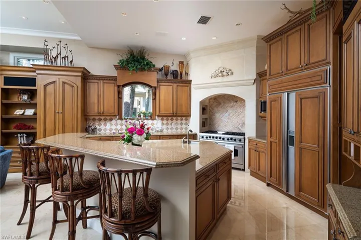 Kitchen with light stone counters, a large island with sink, high end appliances, a breakfast bar, and recessed lighting