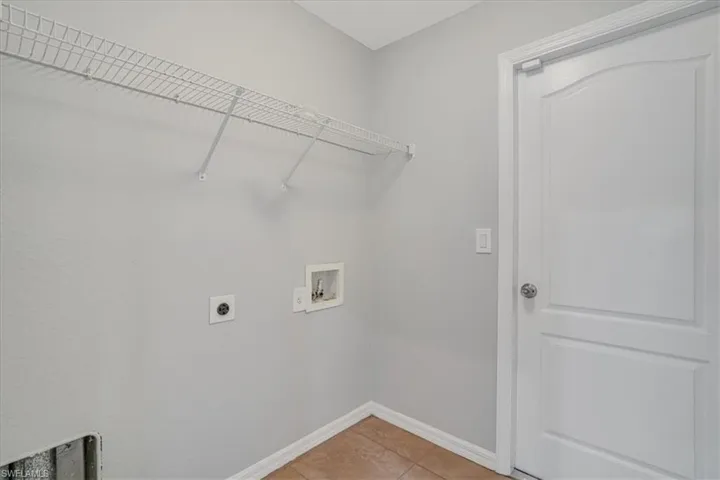 Clothes washing area with hookup for a washing machine, tile patterned flooring, and electric dryer hookup