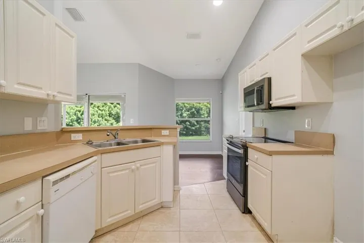 Kitchen with appliances with stainless steel finishes, kitchen peninsula, light tile patterned floors, lofted ceiling, and sink