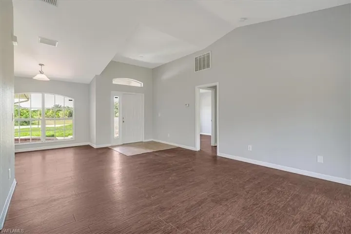 Empty room with vaulted ceiling and dark wood-type flooring