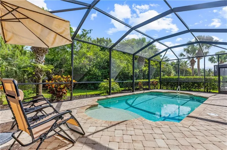Screened outdoor pool area featuring a paver deck, integrated spa, and lush landscaping