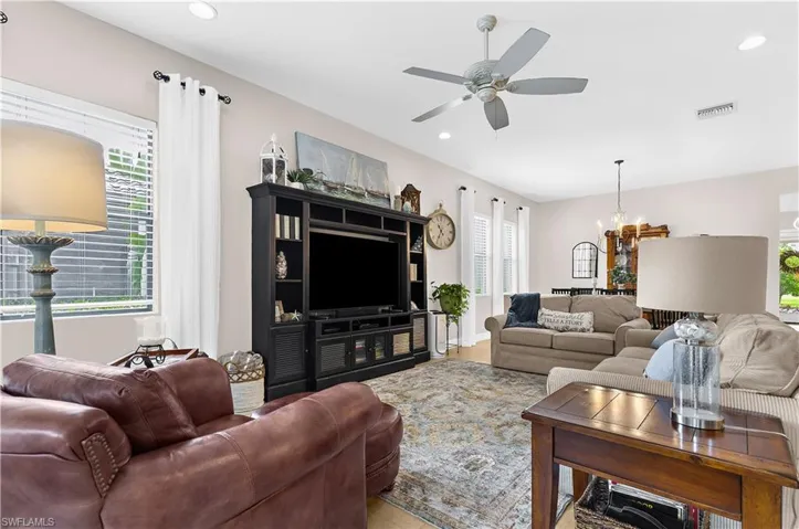 Spacious living area featuring light wood-finish flooring, a contemporary ceiling fan, recessed lighting, and multiple windows with blinds and curtain rods