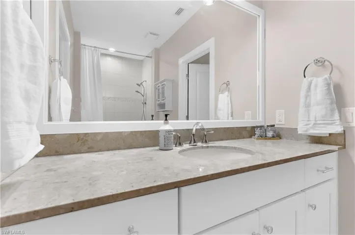 White vanity with ample storage, featuring a light-toned countertop, undermount sink, and polished chrome faucet