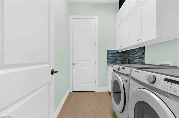 Dedicated laundry area featuring wood-finish flooring, light green wall paint, white shaker-style cabinetry, and a multicolor mosaic tile backsplash