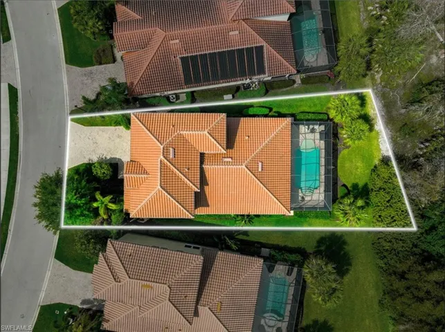 Red tile roof residence featuring a screened pool enclosure, paved driveway, and mature landscaping