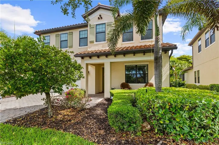 Mediterranean-style exterior featuring a terracotta tile roof, cream stucco facade, decorative window shutters, a covered entry, and mature tropical landscaping