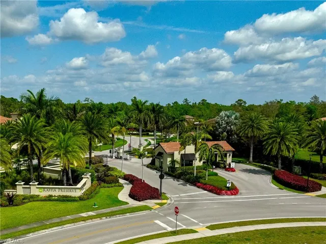 Community entrance featuring a gated entry, lush tropical landscaping, palm trees, and a grand stone-clad sign