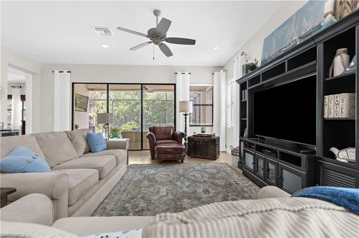 Spacious living area featuring tile flooring, a built-in media console, ceiling fan, recessed lighting, and sliding glass doors leading to a screened lanai