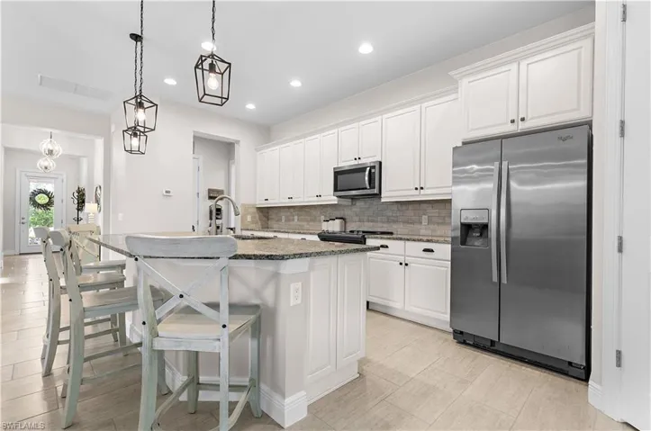 Kitchen featuring a central island with a sink and pendant lighting, white cabinetry, stainless steel appliances, and a tiled backsplash