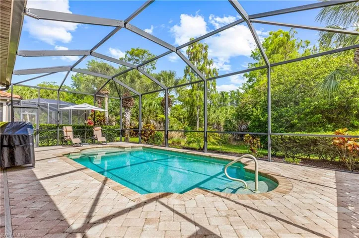 Screened enclosure featuring a swimming pool, integrated spa, and paver decking