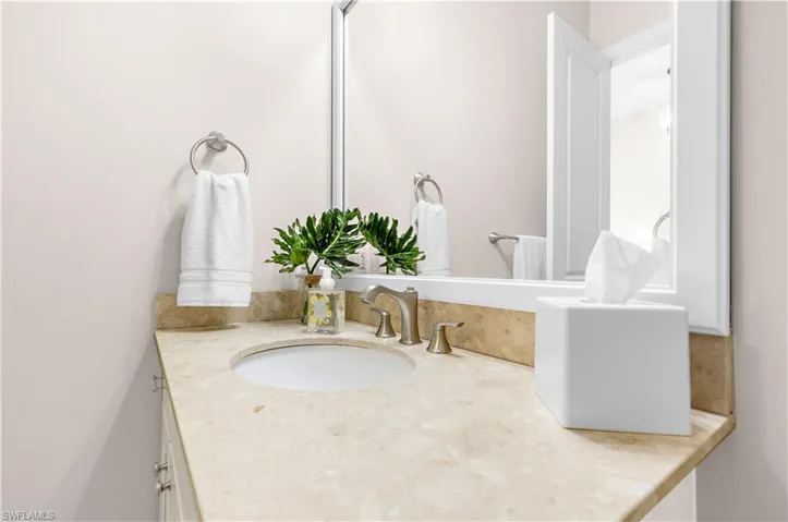Light-toned vanity featuring an undermount sink, brushed nickel faucet, and a stone countertop with a matching backsplash