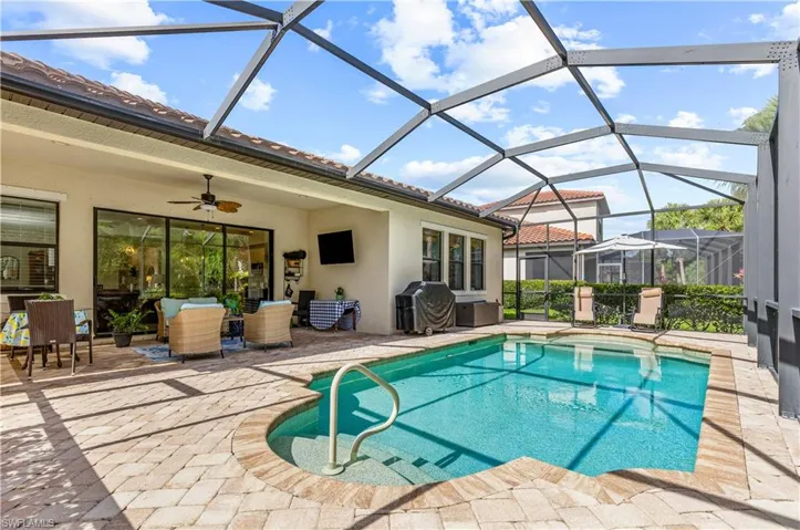 Screened lanai featuring a built-in swimming pool with steps and handrail, surrounded by paver decking