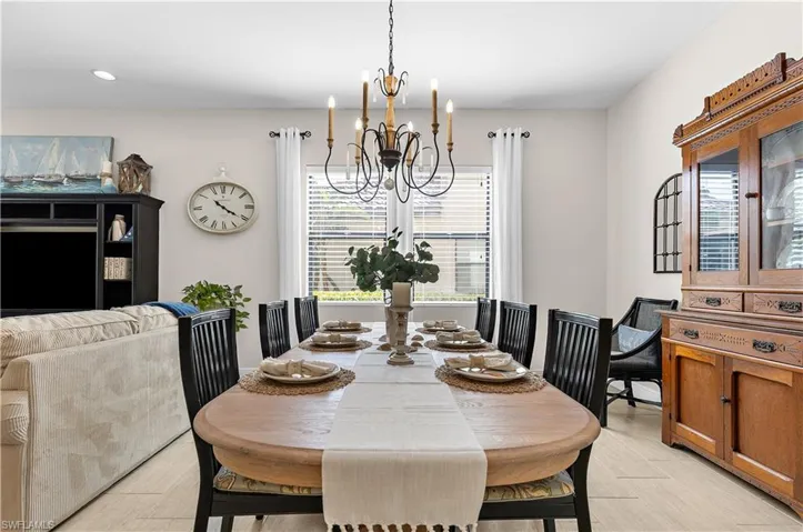Open-concept dining area featuring a chandelier, large window with blinds, light-toned tile flooring, and neutral wall paint