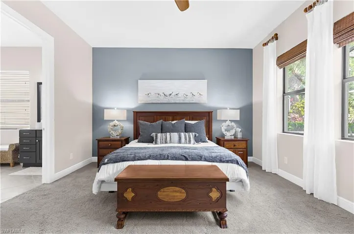 Carpeted bedroom featuring a blue accent wall, two large windows with natural wood blinds, and a ceiling fan