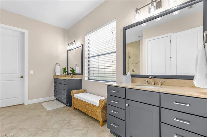 Dual vanity bathroom featuring light-toned tile flooring, gray cabinetry with chrome hardware, and light-toned countertops