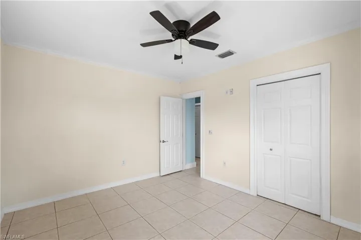 Unfurnished bedroom featuring ornamental molding, light tile patterned flooring, ceiling fan, and a closet