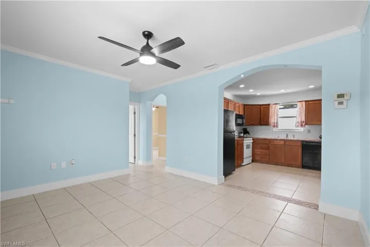 Kitchen featuring arched walkways, light tile patterned flooring, brown cabinets, crown molding, and black appliances