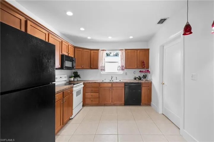 Kitchen with black appliances, brown cabinetry, light tile patterned flooring, pendant lighting, and recessed lighting