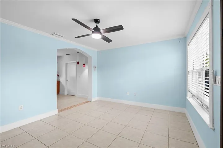 Spare room with ornamental molding, light tile patterned flooring, arched walkways, and ceiling fan