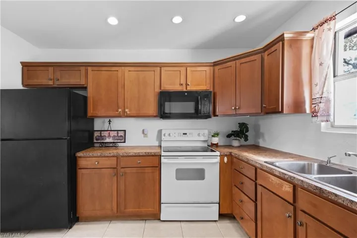 Kitchen featuring black appliances, brown cabinetry, light tile patterned floors, and recessed lighting