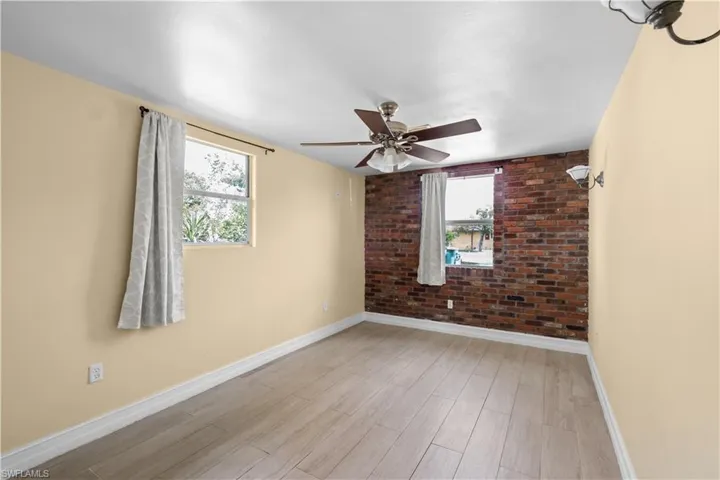 Unfurnished room featuring brick wall, healthy amount of natural light, light wood-type flooring, and a ceiling fan