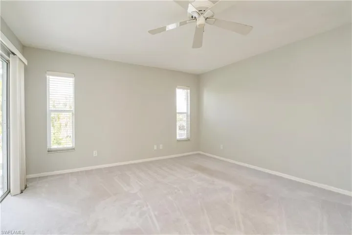 Empty room with a wealth of natural light, light colored carpet, and ceiling fan