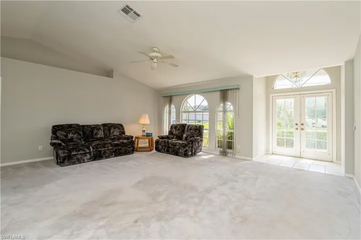 Unfurnished room featuring french doors, vaulted ceiling, light colored carpet, and a healthy amount of sunlight