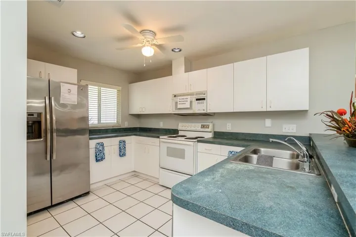 Kitchen with white cabinetry, sink, light tile patterned floors, and white appliances