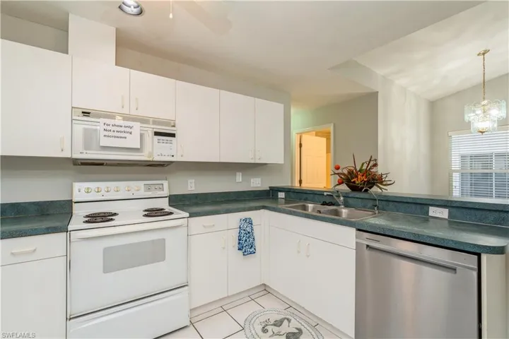 Kitchen featuring white cabinets, an inviting chandelier, light tile patterned flooring, sink, and white appliances