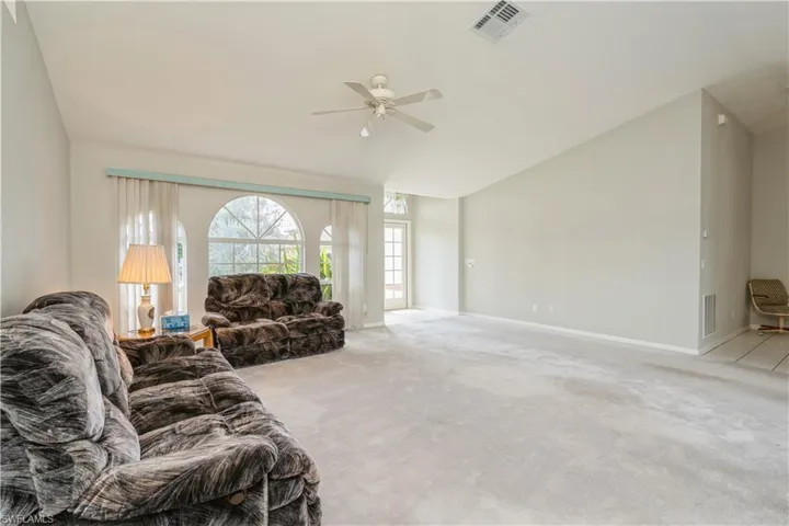 Living room with ceiling fan, lofted ceiling, and light colored carpet