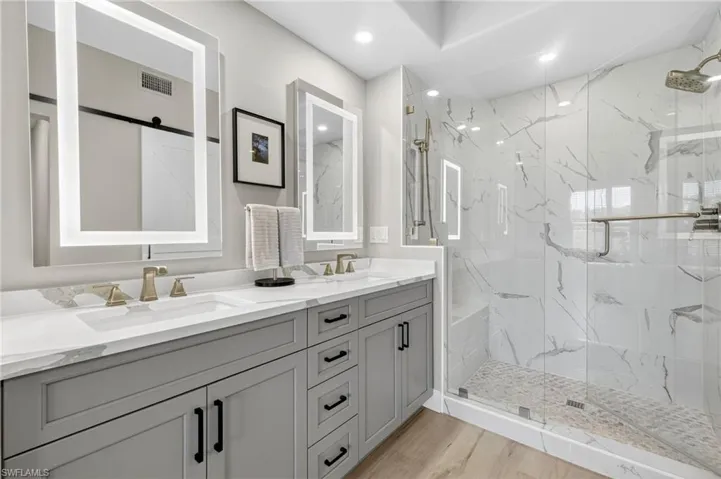 Luxuriously renovated bathroom with shaker cabinetry, quartz countertop, cosmetic lit mirrors with defoggers, pristine walk-in shower and seamless glass doors and modern fixtures