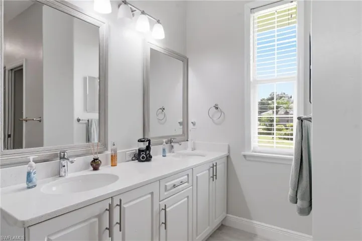 Double vanity featuring white cabinetry, integrated sinks, chrome fixtures, and stone-finish countertops